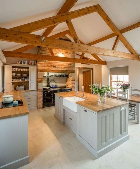 an attic kitchen with wooden beams, a large stove, grey cabinetry, a brick wall and butcherblock countertops is chic