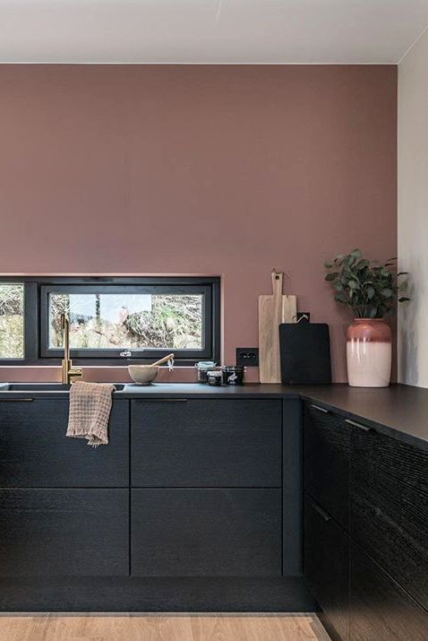 a black minimalist kitchen with mauve walls and a small window as a backsplash is pure elegance and a bold color combo