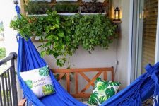 02 a small balcony with artificial grass, a bold blue hammock, potted herbs and simple wooden furniture with pillows