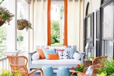 03 a bold coastal porch with a hanging sofa with bright pillows, blue side tables, orange rattan chairs, potted plants and blooms is fun and cool