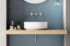 04 a minimalist bathrom with a blue penny tile accent wall, a wooden vanity and a round sink plus a large round mirror