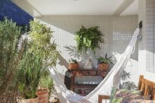 05 a cool balcony with potted shrubs and greenery, with a macrame hammock, a wooden bench with colorful pillows