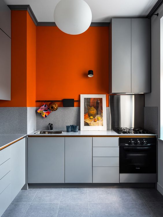 a minimalist kitchen in light grey but with a bold color accent - a statement orange accent wall that enlivens the space