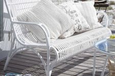 06 a white rattan bench with printed pillows and a table, with a view of the sea and a stack of books