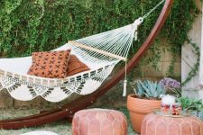 08 a boho backyard space with a living wall, a hammock ona stand, leather poufs, potted plants and blooms and striped rugs