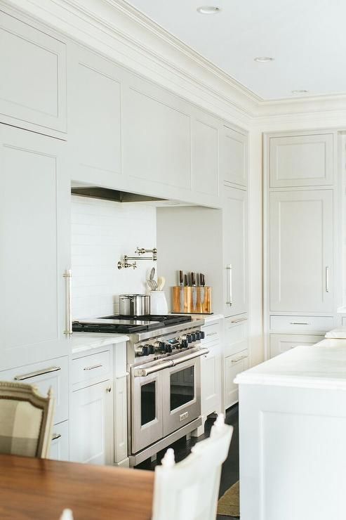 a chic vintage-inspired kitchen in dove grey, with shaker cabinets, a hood hidden inside one of them and a white tile backsplash
