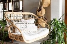 14 a boho porch with a double rattan chair with neutral cushions and pillows, a jute rug, some baskets hanging and potted plants