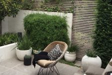 14 a contemporary backyard with a planked screen, with a tiled floor, potted grasses and greenery, a small dining set with pillows and a woven chair
