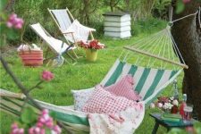 15 a bright summer garden with a striped hammock attached to the trees and printed pillows, some folding chairs and books around
