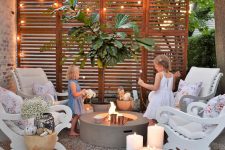 16 a small and inviting backyard with a screen and string lights, with a fire pit and elegant white chairs with pillows, lots of candles and wooden tables