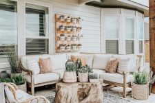22 a farmhouse porch with a wooden corner sofa, a rattan chair, printed pillows, blankets and layered rugs and some potted greenery