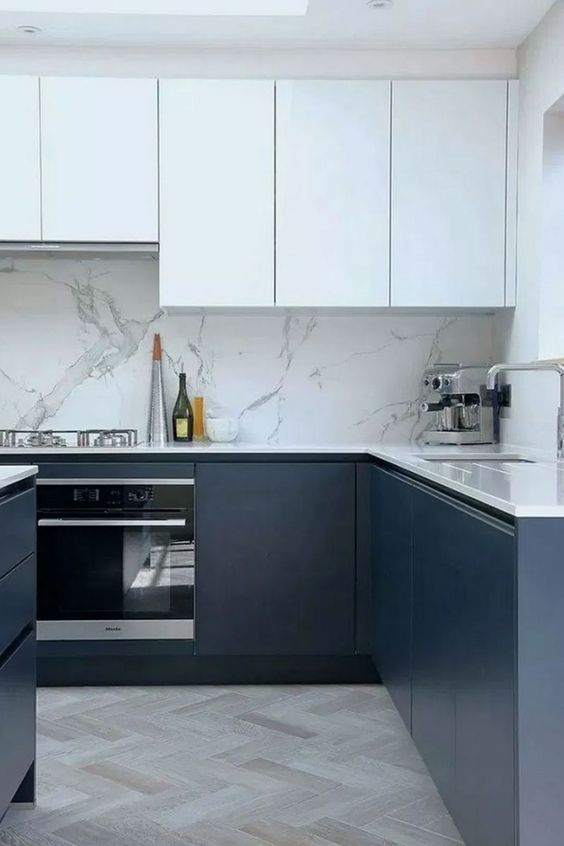 a sophisticated minimalist kitchen with white and navy cabinetry, a white marble backsplash and white countertops is amazing