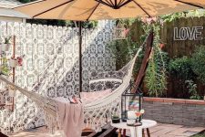 27 a lovely outdoor space with a tiled floor, a hammock on a stand with an umbrella, greenery and a painted fence