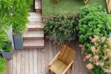 28 a small modern backyard with a raised platform with grass and a lounger, with potted trees, a ladder and a wooden deck with some wooden furniture