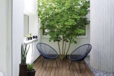 29 a small modern backyard with a wooden deck, navy woven chairs, a living tree and some potted plants is cool and chic