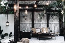 30 a small tropical backyard with a gazebo, an upholstered bench and a low table, a chest for storage, string lights and pretty poufs