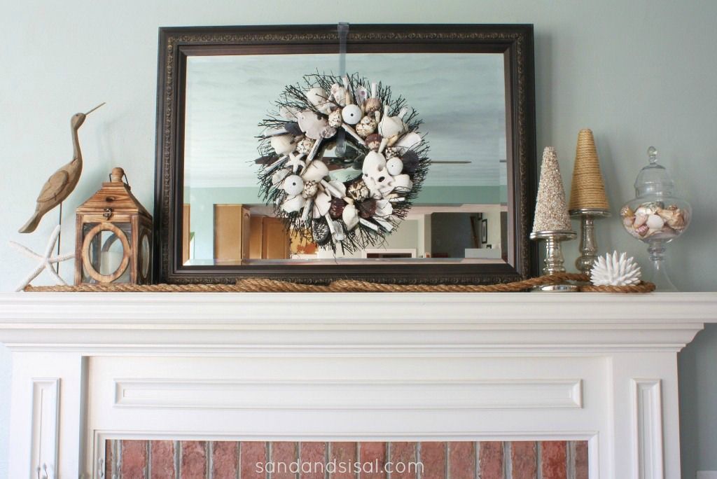 a beachy mantel with a seashell and starfish wreath, a wooden candle lantern and a rope, seashells in a jar
