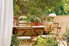 a beautiful Mediterranean terrace with a simple woodne dining seat, potted plants and blooms, a jute pouf is very welcoming