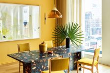 a bold dining room with a yellow accent wall, a terrazzo dining table, yellow chairs and curtains plus a yellow and amber pendant lam[