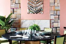 a bold dining room with pink walls and a ceiling, a round black table, green chairs and some potted plants plus a bold artwork on the wall