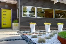 a bright and cool modern front yard with pebbles, tiles, grass balls and bold greenery in tall planters plus a planter with a neon house number