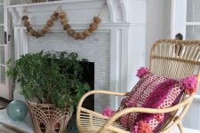 a bright coastal mantel with a wooden bead garland, a potted plant, some seashells, a buoy and a bright photo of the coast