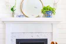 a bright summer mantel with a round mirror, potted greenery and blooms, corals and antlers on the wall