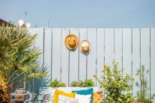 a bright summer terrace with a blue pallet loveseat and printed pillows, potted plants and trees, various Moroccan lanterns