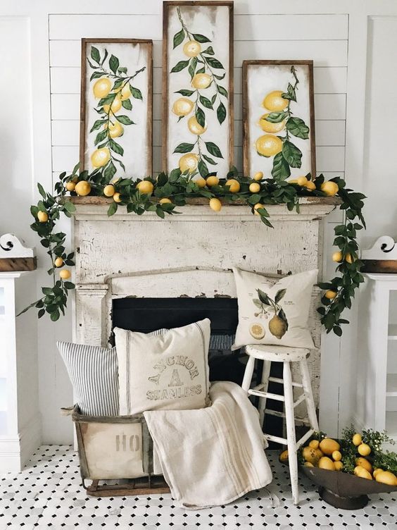a cheerful summer mantel with a lush garland of greenery and lemons and matching artworks, a pack of lemons and some pillows