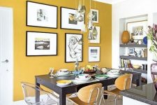 a chic and refined dining room with a mustard accent wall, a black table and mismatching chairs, a cluster of pendant lamps