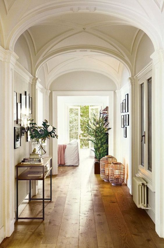 a chic hallway with white walls and arched ceilings, with light-stained hardwood floors and lovely gallery walls
