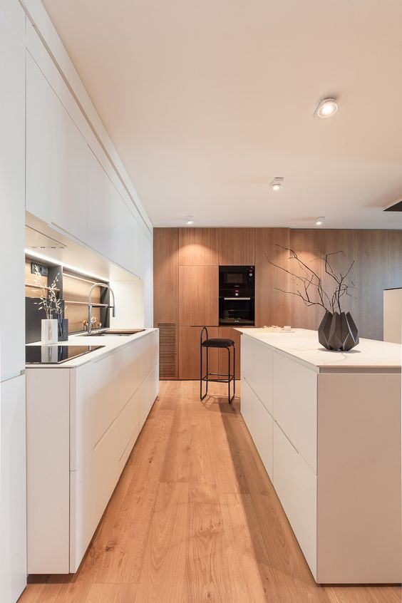 a chic minimalist white kitchen with sleek cabinets, stained ones with appliances, a mirror backsplash and shiny fixtures