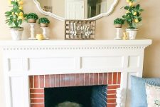 a classic farmhouse summer mantel with potted greenery, faux lemons, a mirror and a box with greenery in the fireplace