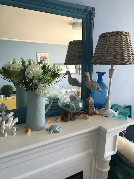 a coastal and farmhouse mantel with a sea gull, a faux turtle, a coral, some seashells, some blooms and a woven lamp