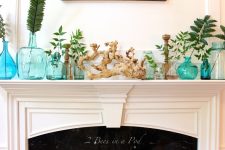 a coastal-inspired mantel with blue vases, jars and bottles and a single leaf in each of them, driftwood and candles is cool
