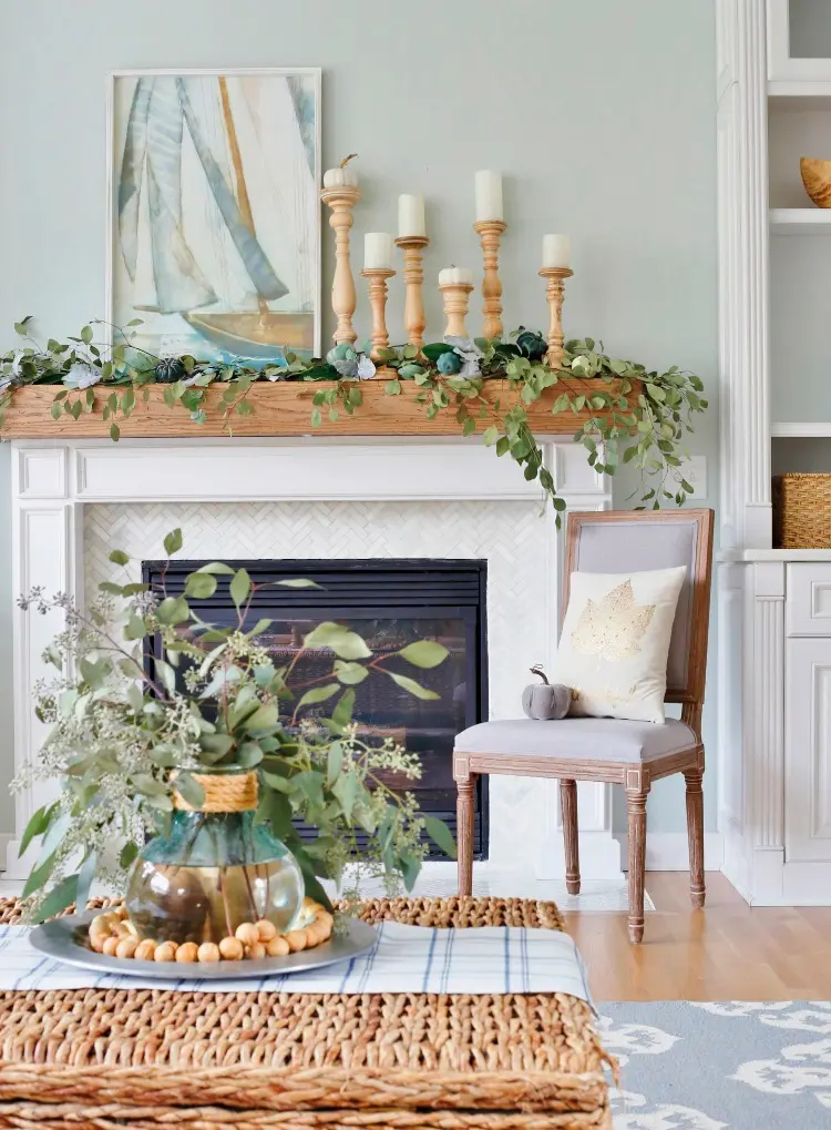 a coastal mantel covered with greenery, with blue pumpkins to embrace the fall, a coastal artwork and candles in wooden candleholders