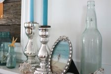 a coastal mantel with blue candles, bottles and jars, silver candleholders, a photo on the beach is personalized