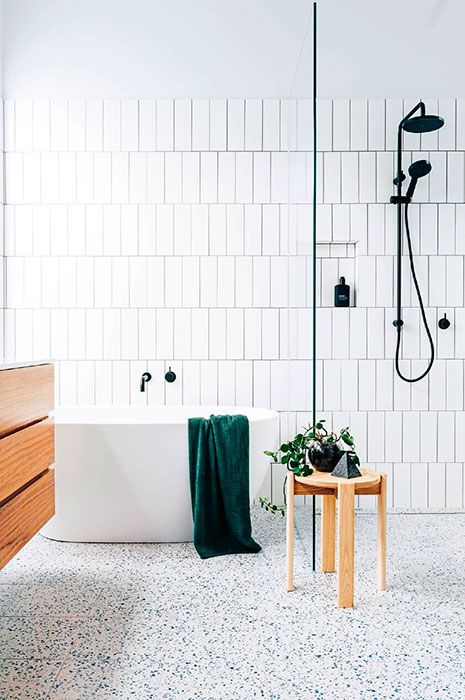 a contemporary bathroom with white skinny tiles and a bright terrazzo floor, a floating vanity and a wooden stool plus black fixtures