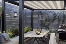 a contemporary outdoor dining space with a sleek built-in bench, a lightweight table and black chairs, a grill and a floor lamp by its side