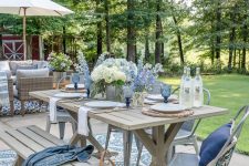 a cool coastal outdoor dining space with a trestle table and a bench, metal chairs, blue textiles, blooms and glasses is amazing