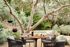a cool contemporary dining space located by a tree with pendant planters, with a round table and black rattan chairs is cool