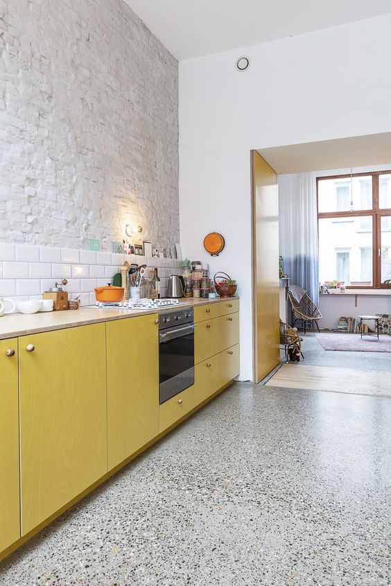 a cool kitchen with black and white terrazzo flooring, white brick and tile walls, mustard kitchen cabinets is amazing