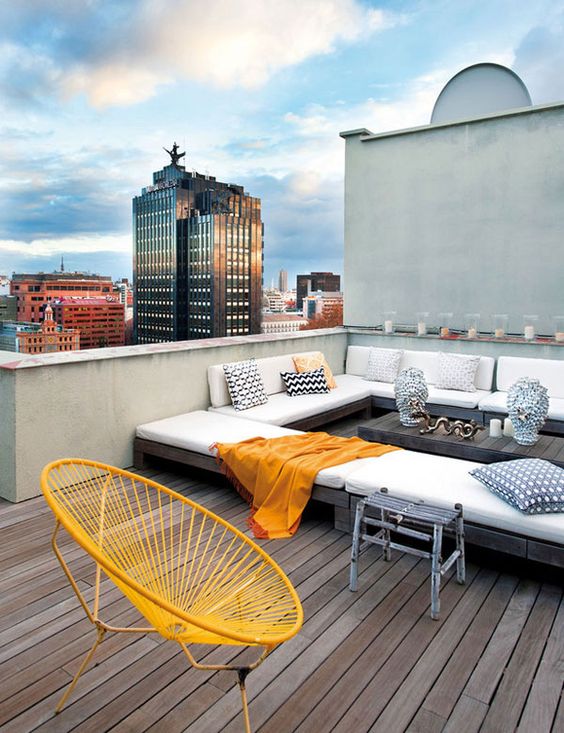 a cool modern rooftop terrace with a wooden deck, a large sectional, some cool chairs and printed pillows is welcoming