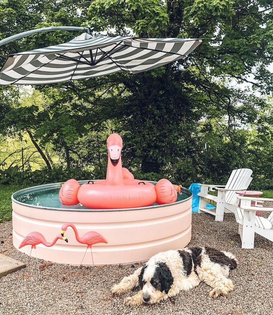 a cool pool space with a stock tank pool in blush, with a flamingo float, flamingos and a striped umbrella and outdoor chairs