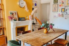 a cozy eclectic dining room with a yellow accent wall and a yellow fireplace, a wooden table, mismatching chairs and benches and a bold gallery wall
