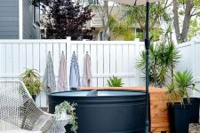 a cozy pool nook with a black stock tank pool, a wooden deck, potted plants, an umbrella and a woven chair and a side table