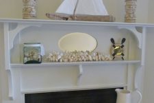 a creative coastal mantel with seashells, a boat, carved wooden candle holders and a jar with seashells is very cool
