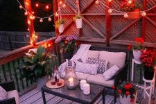 a deck with dark woven furniture, potted blooms, string lights over the space and printed pillows is cozy and welcoming