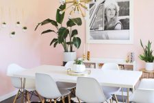 a dreamy dining space with light pink walls, a hairpin leg table and white chairs, potted plants and a gold sunburst chandelier
