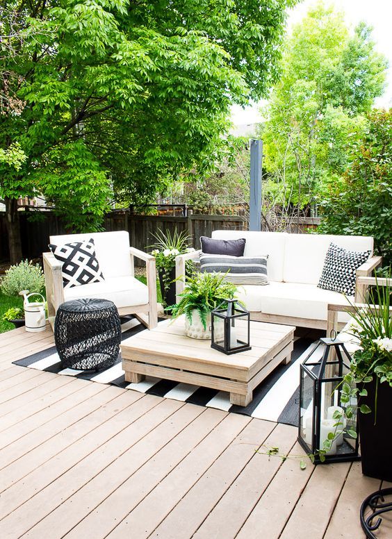 a fresh summer deck with planked outdoor furniture, printed pillows, candle lanterns, printed rugs and lots of greenery to refresh the space